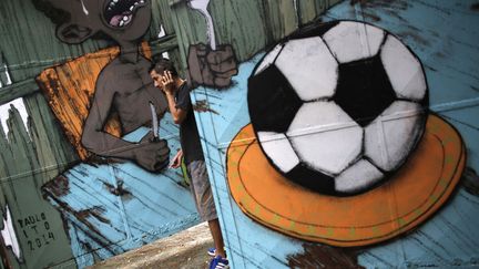 L'artiste br&eacute;silien&nbsp;Paulo Ito en conversation t&eacute;l&eacute;phonique devant son d&eacute;sormais c&eacute;l&egrave;bre graffiti r&eacute;alis&eacute; sur la porte d'une &eacute;cole de Sao Paulo (Br&eacute;sil), le 22 mai 2014. (NACHO DOCE / REUTERS)