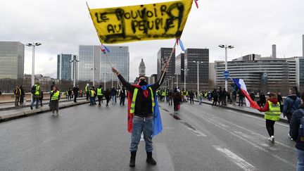 Un "gilet jaune" tient une banderole "Le pouvoir au peuple" devant d'autres manifestants, lors de la 11e journée de mobilisation des "gilets jaunes", le 26 janvier 2019 à Paris.&nbsp; (CHRISTOPHE ARCHAMBAULT / AFP)