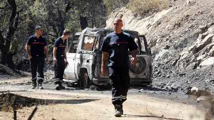 Des pompiers marchent près d'une carcasse de voiture, le 25 juillet 2017 à Ramatuelle (Var). (VALERY HACHE / AFP)