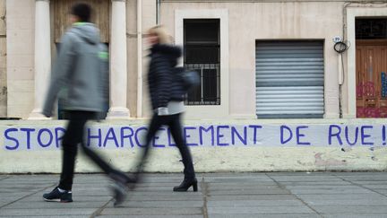 Des passants dans une rue marchent devant une bannière "stop au harcèlement de rue" à Marseille (Bouches-du-Rhône), le 23 novembre 2019. (CLEMENT MAHOUDEAU / AFP)