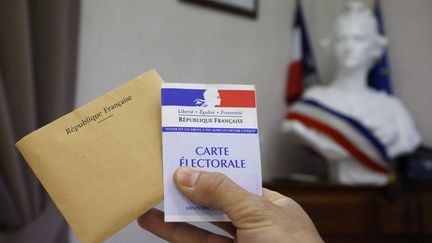 Un électeur tient un bulletin de vote et une carte électorale, le 27 juin 2021, à&nbsp;Etaples (Pas-de-Calais). (LUDOVIC MARIN / AFP)