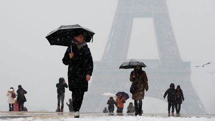 Promenant&nbsp;près de la tour Eiffel, des passants se protègent de la neige avec des parapluies, à Paris. (GONZALO FUENTES / REUTERS)