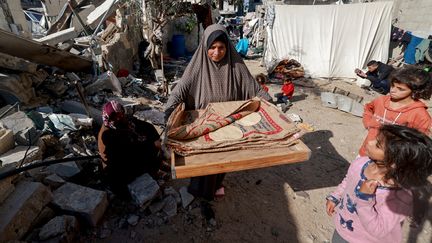 Une femme transportant du pain à côté de maisons détruites à Rafah, dans le sud de la bande de Gaza, le 11 décembre 2023, au milieu des combats continus entre Israël et le Hamas. (MOHAMMED ABED / AFP)