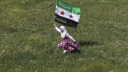 Une r&eacute;fugi&eacute;e&nbsp;syrienne court avec un drapeau de l'opposition lors d'une manifestation devant l'ambassade de Syrie &agrave; Amman (Jordanie), le 13 avril 2012. (ALI JAREKJI / REUTERS)