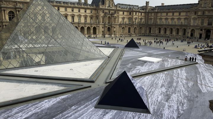 Le trompe-l'œil réalisé par l'artiste JR pour les 30 ans de la pyramide du Louvre en cours de pose, le 27 mars 2019. (ANNE CHÉPEAU / RADIO FRANCE)