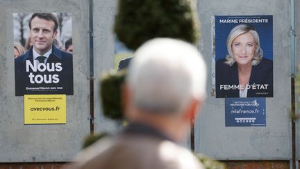 Un homme passe devant des affiches de campagne des candidats au deuxième tour de l'élection présidentielle à Denain (Nord), le 11 avril 2022. (LUDOVIC MARIN / AFP)