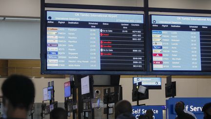 Des voyageurs passent devant un tableau d'affichage, montrant de nombreux vols annulés, à l'aéroport&nbsp;OR Tambo International de Johannesbourg en Afrique du Sud.&nbsp; (PHILL MAGAKOE / AFP)