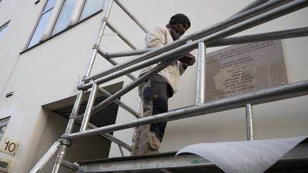 Un ouvrier fixe, le 4 janvier 2016 à Paris, la plaque commémorative sur la façade de l'immeuble qui abritait la rédaction de "Charlie Hebdo" lorsqu'elle a été attaquée. (JOEL SAGET / AFP)