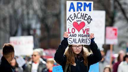 Dans une manifestation contre l'armement des enseignants, à Seattle, le 24 mars 2018, une jeune fille tient une pancarte disant : "Armez les professeurs avec de l'amour et des salaires plus élevés."&nbsp; (LINDSEY WASSON / GETTY IMAGES NORTH AMERICA / AFP)