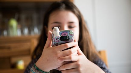 Une jeune adolescente regarde son téléphone portable. (KARINE PERON LE OUAY / HANS LUCAS / AFP)