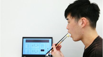 Un étudiant testant les baguettes électriques. (Société Kirin / Université Meiji)