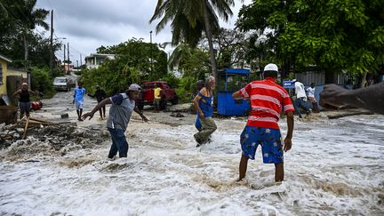 Des personnes franchissent un axe inondé par de l'eau de mer après le passage de l'ouragan Béryl dans le secteur de Saint James, près de Bridgetown (La Barbade), le 1er juillet 2024. (CHANDAN KHANNA / AFP)