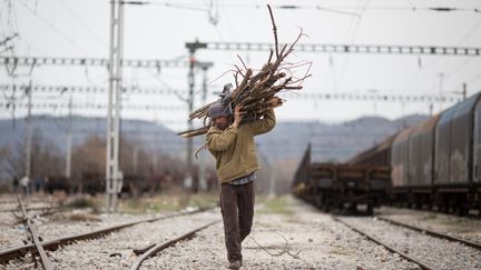 Un homme porte du bois pour faire un feu. Il traverse l'ancienne gare de frêt d'Idomeni pour rejoindre le camp de réfugiés, le 6 mars 2016. (KAY NIETFELD / DPA)