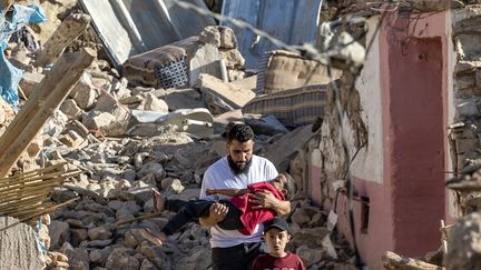 Un homme porte un garçon alors qu'il passe devant des maisons détruites après un tremblement de terre dans le village de montagne de Tafeghaghte, au sud-ouest de Marrakech, le 9 septembre 2023. Le séisme a tué plus de 2 000 personnes. (FADEL SENNA / AFP)