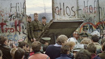 Des habitants de Berlin-Ouest observent des soldats d'Allemagne de l'Est démolir le mur de Berlin, le 11 novembre 1989. (GERARD MALIE / AFP)