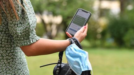 Une femme tenant son smartphone à la main et son masque sanitaire au poignet. Photo d'illustration. (FRANKHOERMANN/SVEN SIMON / SVEN SIMON)