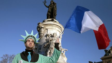 Un homme d&eacute;guis&eacute; en statue de la Libert&eacute; tient un drapeau fran&ccedil;ais place de la R&eacute;publique &agrave; Paris, quelques heures avant le d&eacute;but de la marche r&eacute;publicaine. (JOEL SAGET / AFP)