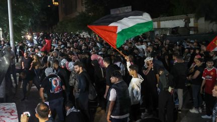 Devant l'ambassade française à Beyrouth (Liban), des dizaines de personnes agitent le drapeau palestinien, tôt le matin du 18 octobre 2023, au lendemain de la frappe meurtrière qui a touché l'hôpital de Gaza. (ANWAR AMRO / AFP)