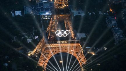 Une vue aérienne de la Tour Eiffel et des anneaux olympiques illuminés lors de la cérémonie d'ouverture des Jeux Olympiques de Paris 2024, à Paris, le 26 juillet 2024. (LIONEL BONAVENTURE / POOL)