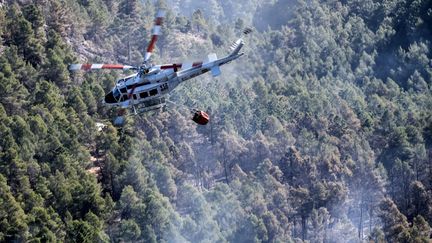 Un hélicoptère survole une forêt près du village de Los Peiros, le 25 mars 2023, pour lutter contre un incendie de forêt qui a débuté près de Villanueva de Viver, à quelque 90 kilomètres au nord de Valence. (JOSE JORDAN / AFP)