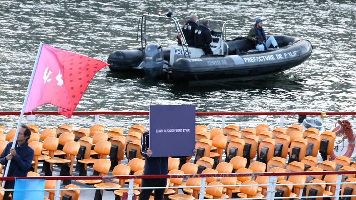 Des membres de l'organisation de Paris 2024, munis de drapeaux et de pancartes, répètent leurs gammes lors du test technique sur la Seine, le 17 juillet 2023. (DELPHINE GOLDSZTEJN / MAXPPP)