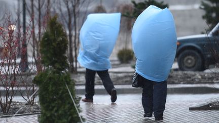 Des membres du staff se prot&egrave;gent de la pluie avec des sacs en plastique, le 18 f&eacute;vrier 2014. (LEON NEAL / AFP)