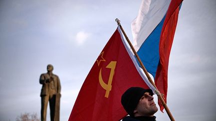 16 mars 2014. Un habitant de Crimée brandit un drapeau de l'Union soviétique, sous les yeux de Lénine, à Simféropol. Derrière le drapeau rouge, un drapeau russe. (DIMITAR DILKOFF / AFP)