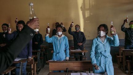 Des élèves malgaches brandissent des bouteilles de Covid-Organics, une tisane présentée par le président comme un remède contre le coronavirus (Antatanarivo, le 23 avril 2020).&nbsp; (RIJASOLO / AFP)