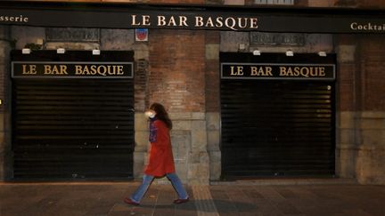 Une femme marche dans la rue à Toulouse (Haute-Garonne) et passe devant un bar fermé, alors que la ville a mis en place un couvre-feu, le 17 octobre 2020. (XAVIER DE FENOYL / MAXPPP)