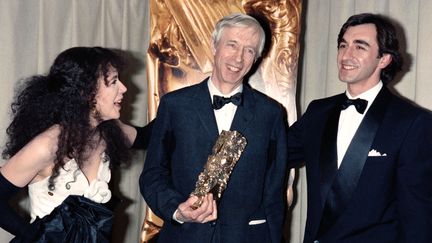 Michel Deville prend la pause après avoir reçu le César du meilleur réalisateur, entouré des acteurs Carole Laure et Christophe Malavoy, le 22 février 1986, à Paris. (MICHEL GANGNE / AFP)