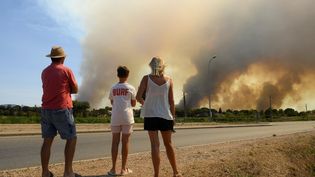 Des vacanciers observent un feu de forêt, le 18 août 2021, à La Garde-Freinet (Var). (NICOLAS TUCAT / AFP)