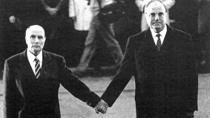 Le président François Mitterrand et le chancelier Helmut Kohl se donnent la main, le 22 septembre 1984 à Verdun, alors que les hymnes nationaux des deux pays sont interprétés par un orchestre militaire, lors de la cérémonie hommage aux morts de 14-18. (BETTMANN ARCHIVE / GETTY IMAGES)