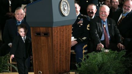 Un petit gar&ccedil;on se cache derri&egrave;re le pupitre du pr&eacute;sident des Etats-Unis lors d'une c&eacute;r&eacute;monie de remise de m&eacute;dailles &agrave; la Maison Blanche &agrave; Washington (Etats-Unis), le 11 f&eacute;vrier 2013. (WIN MCNAMEE / GETTY IMAGES)