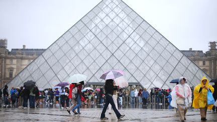 Des touristes se pressent sous la pyramide du Louvre, sous la pluie, le 24 juin 2012 &agrave; Paris. (ALEXANDER KLEIN / AFP)