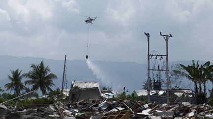 Un hélicoptère asperge un quartier de Palu (Indonésie) avec du liquide désinfectant, le 18 octobre 2018. (YUSUF WAHIL / AFP)