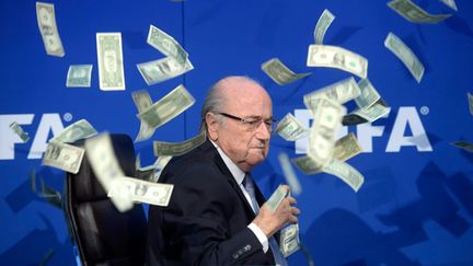 &nbsp; (Sepp Blatter, le président démissionnaire de la Fifa, a été aspergé de faux dollars par un humoriste britannique qui s'est introduit à la conférence de presse © Maxppp)