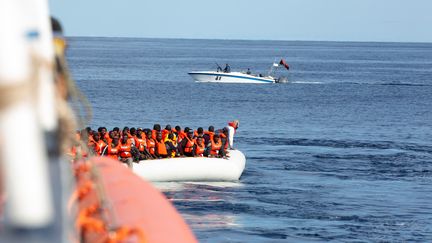 Des migrants secourus en Méditerranée par l'"Alan Kurdi", navire humanitaire de l'ONG allemande Sea-Eye, le 26 octobre 2019. Au second plan,&nbsp;un bateau des gardes-côtes libyens. (HANDOUT / REUTERS)