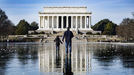 Un homme et un enfant marchent sur un plan d'eau gelé au pied du Lincoln Memorial, à Washington (Etats-Unis), le 26 décembre 2022. (JIM WATSON / AFP)