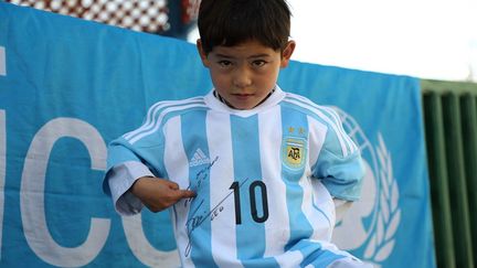 Murtaza est fier de poser avec son maillot flambant neuf aux couleurs de l'équipe nationale d'Argentine. Fou de joie, du haut de ses cinq ans, il a tapé le ballon sur un terrain dans la capitale afghane où il était venu la veille avec son père pour recevoir ses deux maillots dédicacés par sa star préférée. «Con mucho cariño" (avec toute mon affection), peut-on lire sur l'un des maillots aux couleurs de l'équipe argentine et l'autre du Barça qui lui ont été remis par une porte-parole de l'Unicef local. L'Afghanistan, où le Barça est tout aussi populaire que le Real Madrid, a été très ému par l'histoire du petit Murtaza. Dautant que l'enfant vit à Ghazni, une province de l'est de l'Afghanistan où les rebelles talibans sont très présents. De plus, il est issu de la minorité hazara, depuis longtemps discriminée et stigmatisée en raison de son appartenance à l'islam chiite, dans un pays à majorité sunnite. L'ambassade d'Espagne à Kaboul réussira peut-être à faire venir le petit Murtaza à Barcelone... (MAHDY MEHRAEEN / UNICEF AFGHANISTAN / AFP)