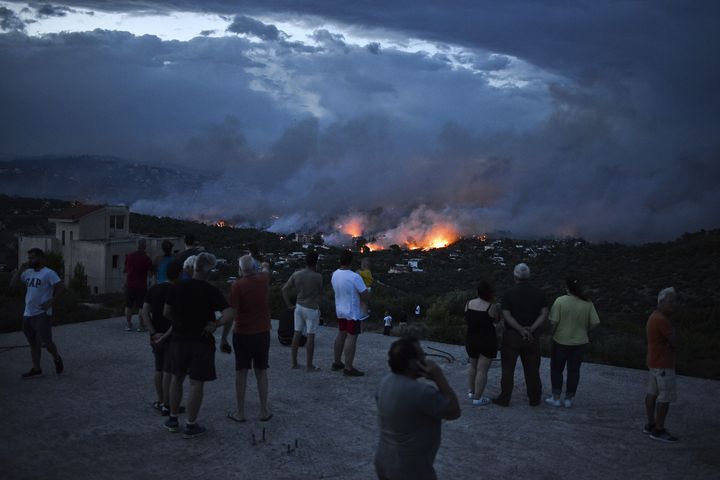 Des personnes regardent le feu à Rafina (Grèce) le 23 juillet 2018. (ANGELOS TZORTZINIS / AFP)