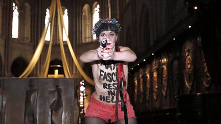 Une membre des Femen&nbsp;braque une arme en plastique devant l'autel de Notre-Dame de Paris, le 22 mai 2013. (KENZO TRIBOUILLARD / AFP)