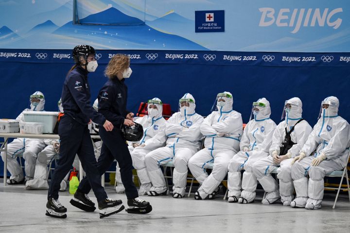 À bonne distance des hockeyeuses, les "minions" de Pékin s'offrent un rare moment de détente pour admirer le match, derrière leurs visières de plexiglas. L'autre grand défi de ces&nbsp;olympiades&nbsp;est d'éviter toute&nbsp;propagation du&nbsp;Covid-19.&nbsp;La Chine a mis au point un protocole sanitaire dantesque et créé une&nbsp;bulle tout autour des structures olympiques... et de leurs bénévoles. (ANNE-CHRISTINE POUJOULAT / AFP)