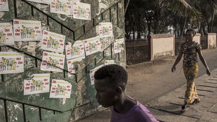 Des habitants de Conakry (Guinée) se baladent devant un mur où des affiches "Oui au référendum" ont été collées, le 26 février 2020. (JOHN WESSELS / AFP)