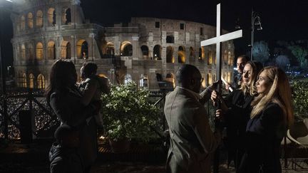 Le Chemin de Croix présidé par le pape à Rome, le 15 avril 2022. Irina (deuxième à droite), une Ukrainienne, et Albina (à droite), une Russe, remettent la croix à une famille de migrants. (AFP PHOTO / VATICAN MEDIA)