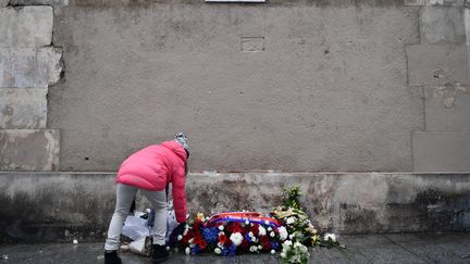 Une enfant dépose des fleurs devant la plaque commémorative installée à l'angle de la rue Alibert et de la rue Bichat, dans le 11e arrondissement de Paris, en hommage aux victimes des attentats, le 13 novembre 2016. (PHILIPPE LOPEZ / AFP)