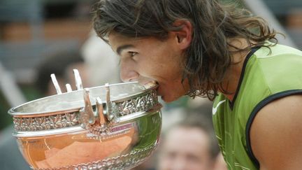 Rafael Nadal croque la coupe des Mousquetaires, après sa première victoire à Roland-Garros, à Paris, le 5 juin 2005, face à l'Argentin Mariano Puerta. (LIONEL CIRONNEAU / SIPA)