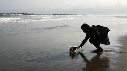 Une jeune fille, dont le p&egrave;re est d&eacute;c&eacute;d&eacute; un an plus t&ocirc;t lors du tsunami,&nbsp;d&eacute;pose un bouquet de fleurs sur la plage d'Arahama (Japon), le 11 mars 2012. (JIJI PRESS / AFP)