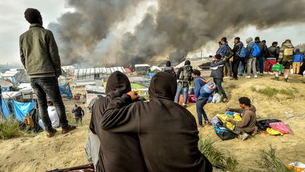 Des migrants observent la fumée s'élever de la "jungle" de Calais (Pas-de-Calais), lors d'une importante opération de démantèlement du camp où résidaient de 6 000 à 8 000 personnes, le 26 octobre 2016. (PHILIPPE HUGUEN / AFP)