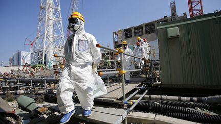 Des journalistes portant des combinaisons et des masques de protection sont escortés par les employés de TEPCO jusqu'au bâtiment commun de la piscine de combustible usé, alors qu'ils se rendent à la centrale nucléaire de Fukushima Daiichi, paralysée par le tsunami à Tokyo Electric Power Co. (TEPCO), dans la préfecture de Fukushima, le 6 mars 2013. (NOBORU HASHIMOTO / CORBIS NEWS / GETTY IMAGES)