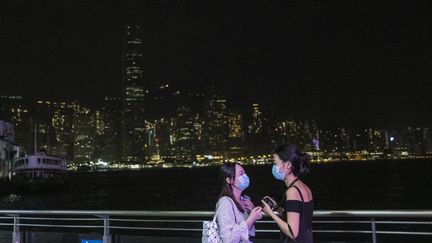 Deux femmes discutent devant le front de mer d'Hong Kong, dont les lumières sont éteintes pour l'Earth Hour, le 27 mars 2021.&nbsp; (VERNON YUEN / NURPHOTO / AFP)